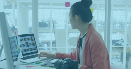 Image of charts processing data over biracial female creative using camera at office. Network, data, finance, digital interface, business, design and communication, digitally generated image.の写真素材