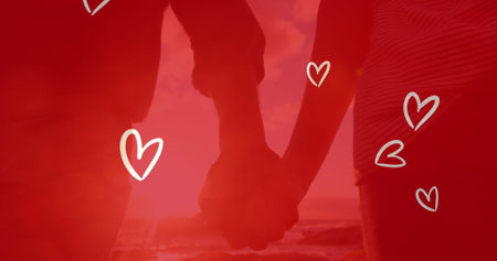 Image of white hearts over caucasian couple holding hands on beach. engagement, marriage, romance and love concept digitally generated image.の写真素材