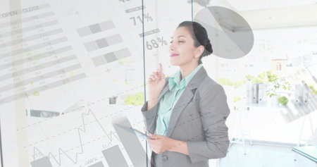 Image of financial data processing over biracial businesswoman using tablet in office. Global finance, business, connections, computing and data processing concept digitally generated image.の写真素材