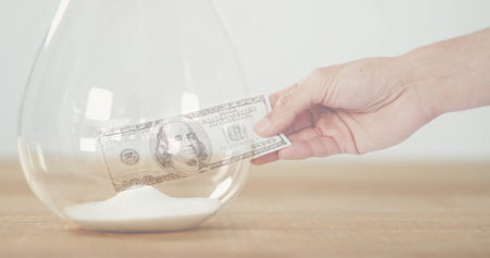 Image of hand holding banknote over hourglass. Business, technology and digital interface concept digitally generated image.の写真素材