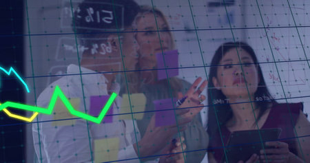 Financial graph image over diverse business team analyzing data on glass board. teamwork,...