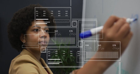 Image of diagrams and data processing over biracial woman taking notes in office. Global business...
