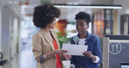 Image of diagram and data processing over biracial female colleagues talking in office. Technology, business and digital interface concept digitally generated image.の写真素材