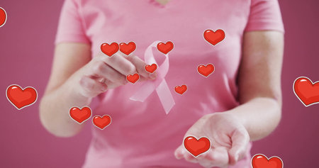 Image of hearts over caucasian woman holding pink ribbon. Global support, cancer and digital interface concept digitally generated image.の写真素材