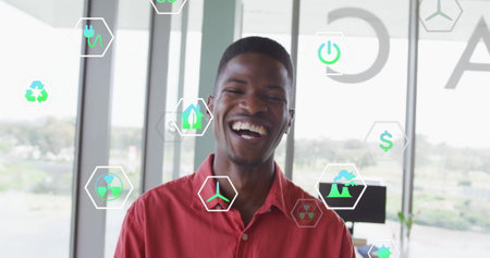 Image of ecology icons over biracial businessman smiling in office. Technology, business and digital...