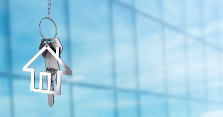 House-shaped keychain with keys image over blurred glass building background. Real estate, keyring,...