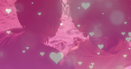 Image of falling hearts over biracial couple embracing at beach. Lifestyle and nature concept...