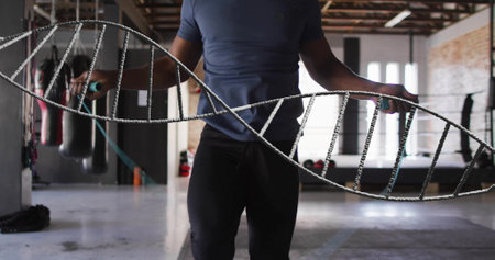 Image of dna strand over biracial man jumping rope at gym. Sport and digital interface concept digitally generated image.の写真素材