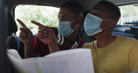 Two biracial male friends wearing face masks using map in cab. backpacking holiday city travel break...