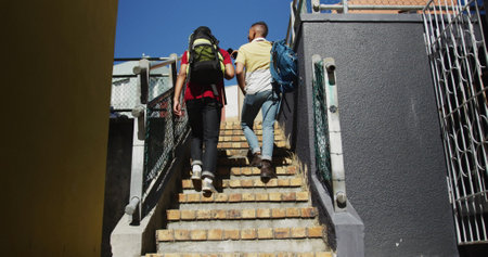 Back view of two biracial male friends walking upstairs and talking. backpacking holiday city travel...