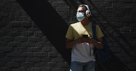 Biracial man wearing face mask and using smartphone in the street. backpacking holiday city travel...