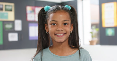 Smiling girl with pigtails in school classroom, looking at camera. Childhood, education, learning, happiness, student, innocence, unaltered, slow motionの写真素材