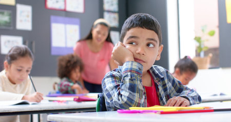 In school, boy daydreaming at desk while classmates and teacher working. Education, classroom, learning, childhood, students, distraction, unaltered, slow motionの写真素材