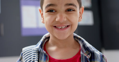 Smiling boy in school classroom wearing plaid shirt and red t-shirt. Education, student, learning,...