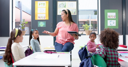 In school, teacher holding tablet and talking to students in classroom. Education, teaching, technology, digital learning, interaction, elementary, unaltered, slow motionの写真素材
