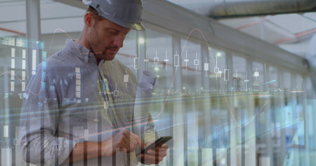 Engineer in hard hat using smartphone with stock market graphs overlaying. Technology, engineering,...