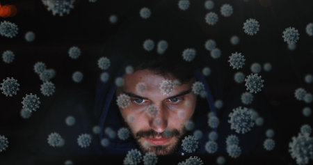Man in hoodie surrounded by digital virus graphics, focused and serious. Cybersecurity, hacking,...