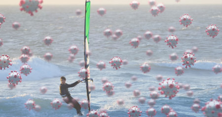 Image of cells floating over caucasian man windsurfing. coronavirus covid-19 pandemic concept digital compositeの写真素材