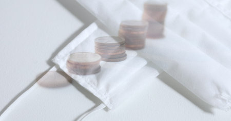 Image of face masks lying on a table over piles of coins. Coronavirus Covid-19 pandemic concept...