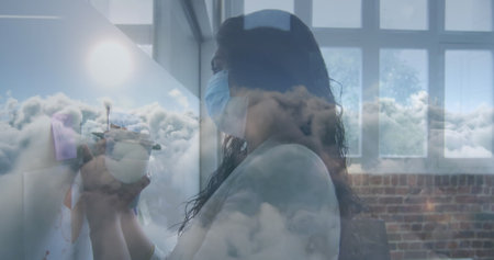 Clouds in blue sky against indian woman wearing face mask writing on white board at office. hygiene...