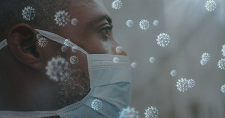 Image of covid 19 cells over close up of african american man wearing face mask. global coronavirus pandemic and protection concept digitally generated image.の写真素材