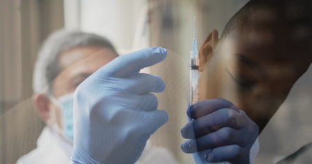 Image of masked gloved doctor flicking vaccination syringe and sleeping child. healthcare and protection during coronavirus covid 19 pandemic, digitally generated image.の写真素材