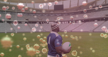 Image of 3d coronavirus cells floating over rugby player holding rugby ball on empty stadium. Global Covid 19 coronavirus pandemic sport concept digitally generated image.の写真素材