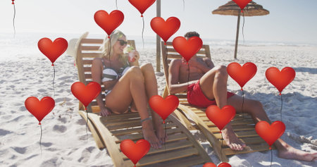 Image of red heart love balloons digital icons over couple in deckchairs with drinks on beach. digital interface, social media and global networking concept digitally generated image.の写真素材