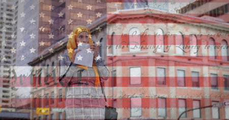 Image of american flag waving over biracial woman in hijab eating takeaway sandwich in city street. american society diversity concept digital composition.の写真素材
