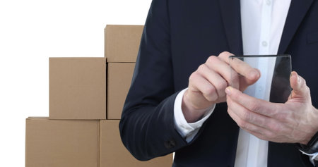 Image of businessman using clear digital tablet with stacks of boxes on white background. global shipping and technology concept digitally generated image.の写真素材