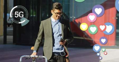 Young man walking with bicycle, using smartphone with 5G connectivity outdoors. Technology,...