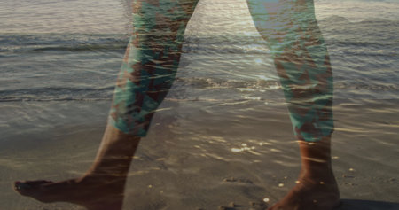 Image of legs of man walking on beach, over sun on sea. holidays and free time, digitally generated...