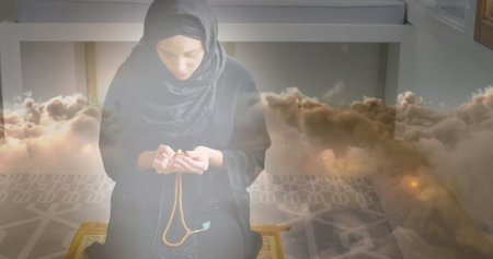 Image of asian woman in hijab praying at home over clouds. spending free time together concept digitally generated image.の写真素材