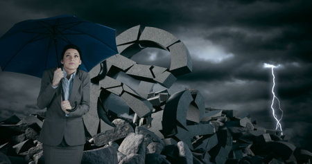 Businesswoman holding umbrella standing among broken currency symbols during storm. Finance, crisis, economy, risk, uncertainty, investmentの写真素材