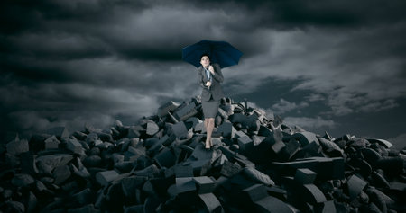 Holding umbrella under stormy sky, businesswoman standing on rubble facing challenges. Determination, resilience, strength, adversity, leadership, ambitionの写真素材