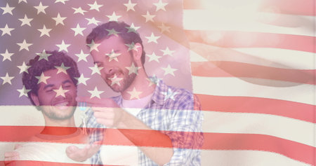 Digital composite of same sex couple smiling and hugging to celebrate new house against animated american flag backgroundの写真素材