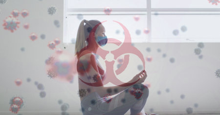 Image of covid-19 cells floating over caucasian woman wearing face mask meditating. Global covid 19pandemic concept digitally generated image.の写真素材