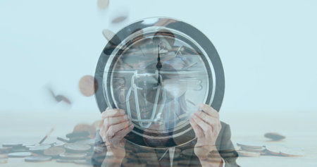 Businessman holding clock against his face against coins falling in background. finance and economy...