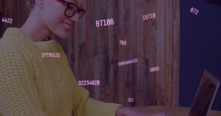 Multiple changing numbers floating against caucasian woman smiling while using laptop. global networking and connection conceptの写真素材