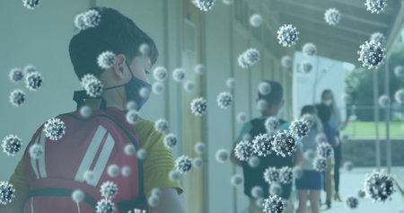 Multiple covid 19 cells floating against school boy wearing face mask standing in a queue at school....