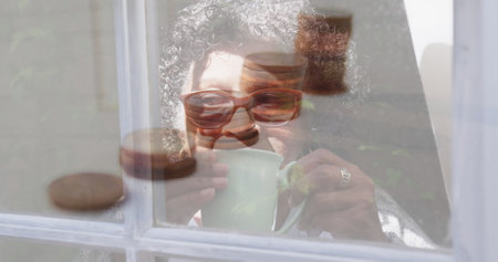 Image of stacks of coins over worried senior woman drinking tea at home. global coronavirus pandemic, medicine and healthcare concept digitally generated image.の写真素材