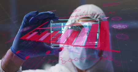 Image of statistics over scientist in ppe suit holding screen with covid 19 cell. global coronavirus pandemic, medicine and research concept digitally generated image.の写真素材