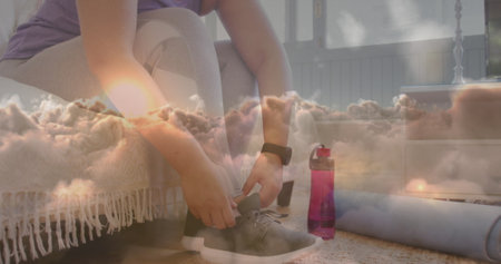 Image of sunset and clouds over woman tying shoe laces, exercising at home. global sports, fitness and active lifestyle concept digitally generated image.の写真素材