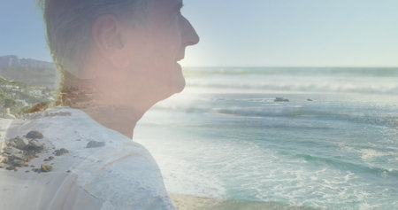 Image of glowing light over portrait of happy senior man by seaside. retirement and senior life concept digitally generated image.の写真素材