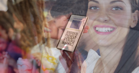 Woman holding a smartphone with qr code on screen against caucasian woman drinking a smoothie. covid-19 vaccination certificate and health pass conceptの写真素材