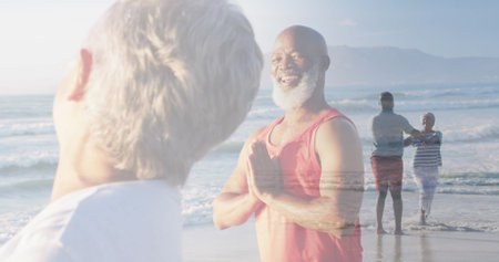 Composite of happy diverse senior couple doing yoga, and dancing on beach. healthy retirement, fitness and wellbeing concept digitally generated image.の写真素材