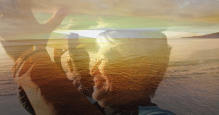 Composite of happy senior couple walking carrying surfboards on heads, and beach at sunset. healthy retirement, fitness and wellbeing concept digitally generated image.の写真素材