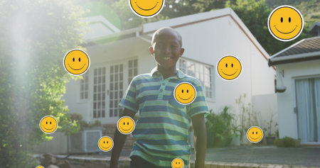 Image of smiley faces over happy african american boy in garden. family, domestic life, love and care concept digitally generated image.の写真素材