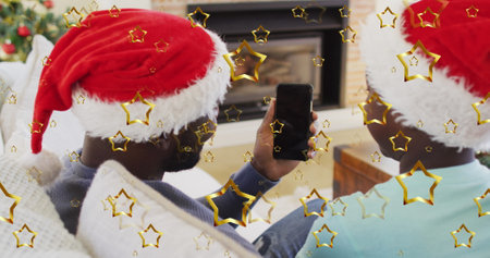 Golden star icons falling against father and son having a imagecall on smartphone during christmas....