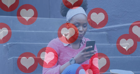 Image of social media heart icons over happy african american woman in street using smartphone. communication technology and social network concept digitally generated image.の写真素材